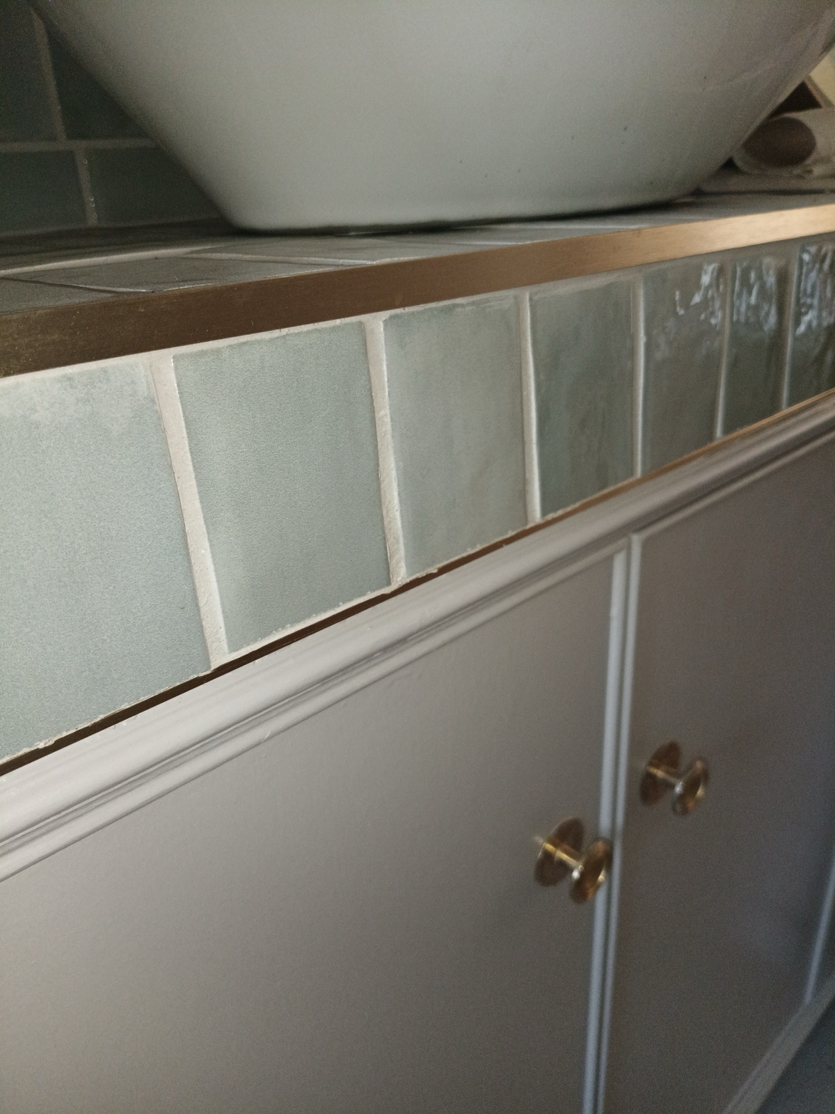 Hand-painted vanity unit with brass knobs beneath sage tiling