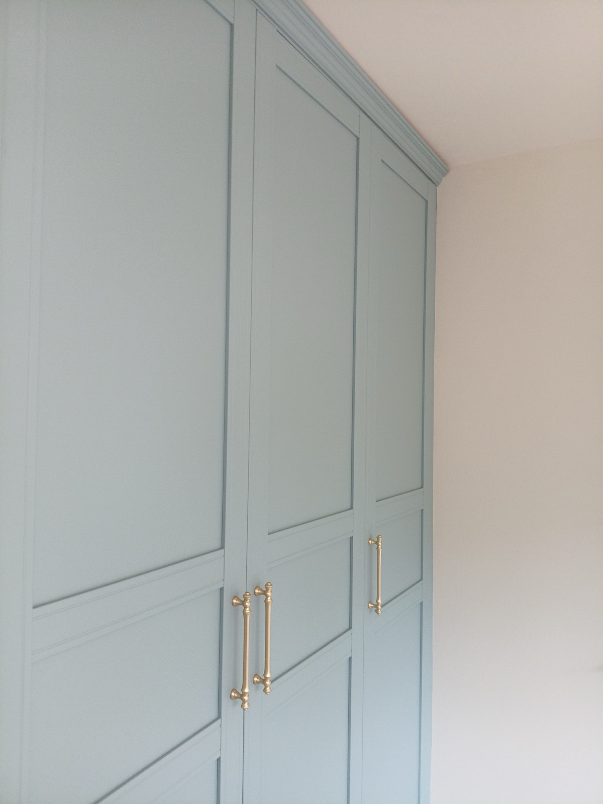 Fitted panelled wardrobes hand-finished in soft blue-grey, with brass handles and a moulded cornice run to the ceiling