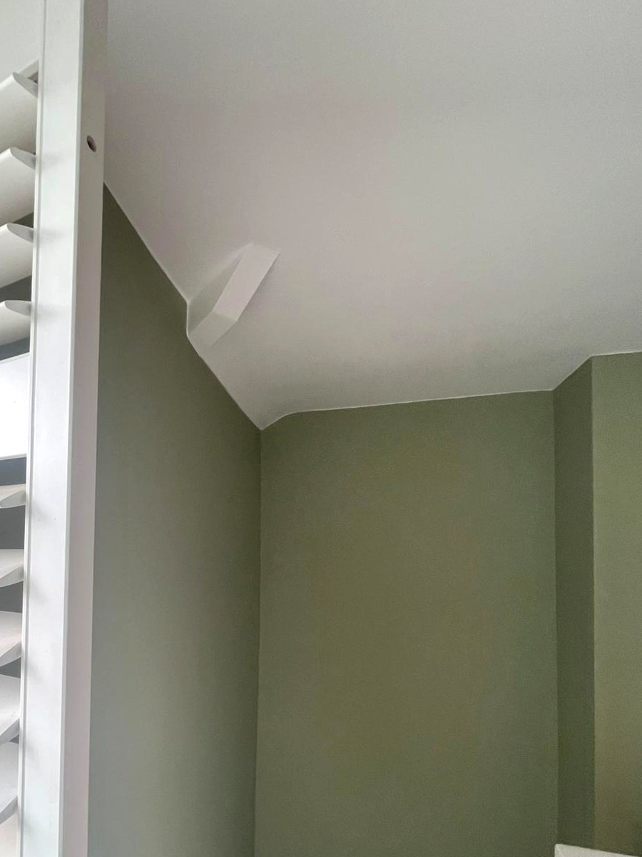 A sloping ceiling in brilliant white cut in against walls in Farrow & Ball Vert de Terre, the line turning cleanly at the structural nib and again at the corner